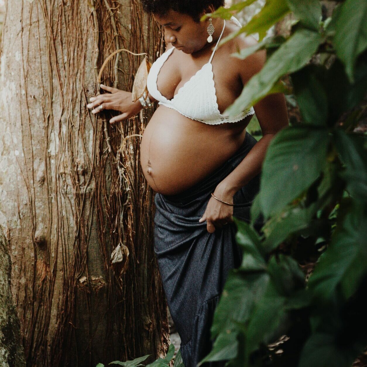 A pregnant black woman stands in the woods